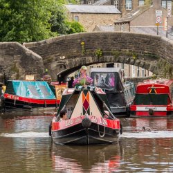 Colourful narrow boats on a river with an old stone bridge in the background