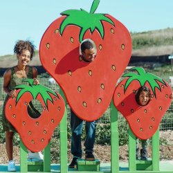 A mother and daughter laughing on the farm and looking at an overflowing bucket of strawberries.