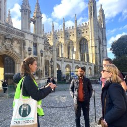 An image of an Uncomfortable Cambridge Tour, with people standing on a quiet stone street listening to a guide.