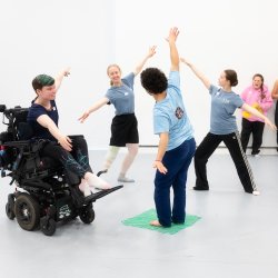 Image features NYB All In! participants dancing Ballet in a light studios with floor length windows.