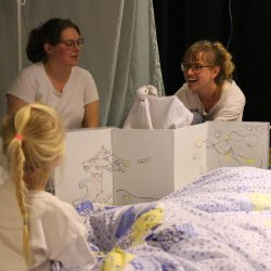 2 performers with a puppet popping up behind a screen being watch by a child