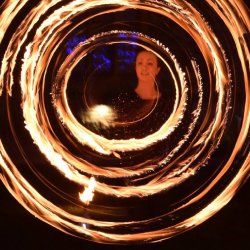 The poster shows a brightly coloured dragon fly, fire artist spinning fire, sculptures and aerial artist and trees are lit with ref, green blue lighting