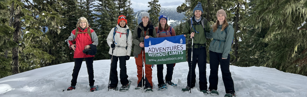 6 people wearing snowshoes pose for a photo with the A-W-L flag on a snowy, tree-lined trail