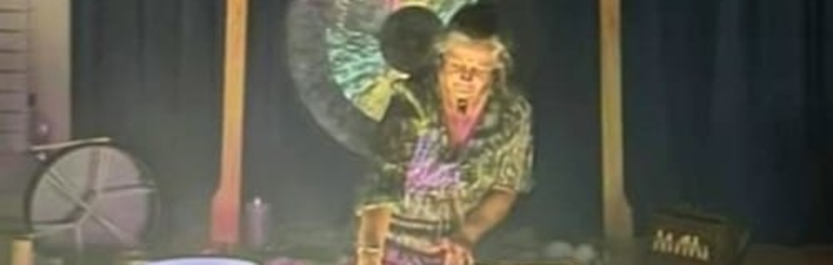 Faye sitting in front of a gong, playing crystal singing bowls