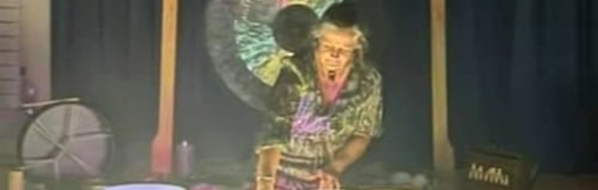 Faye sitting in front of a gong, playing crystal singing bowls