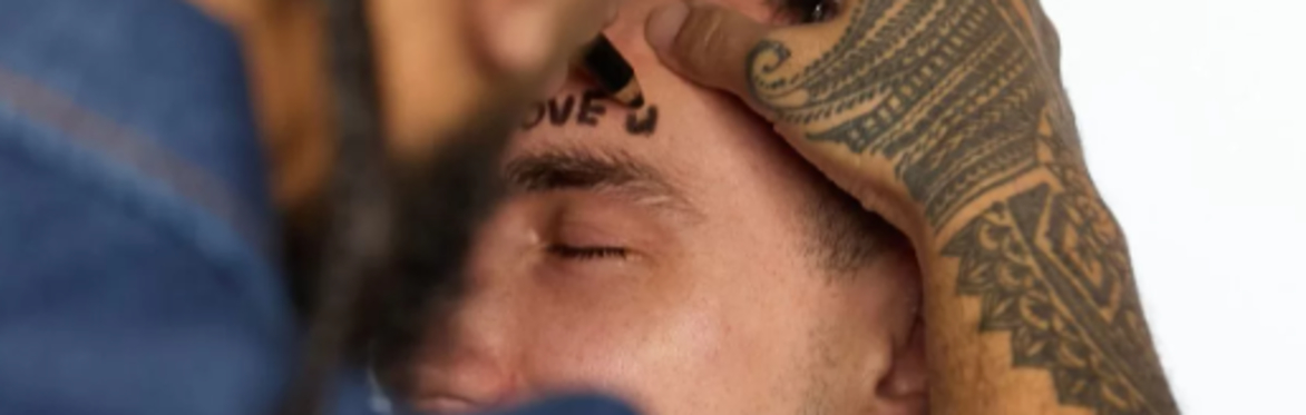 man with tattoos using a pen to write I love you on another mans forehead