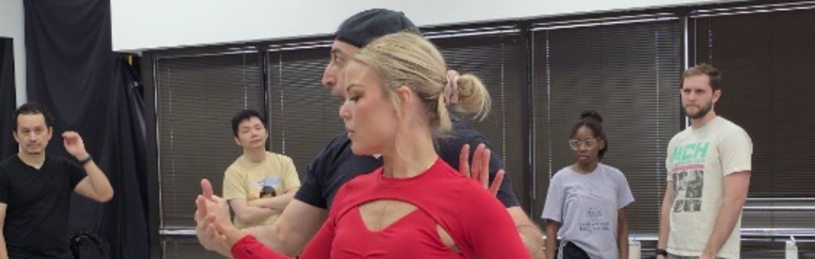 Salsa dancers practicing a partnered turn in a studio while other students watch.