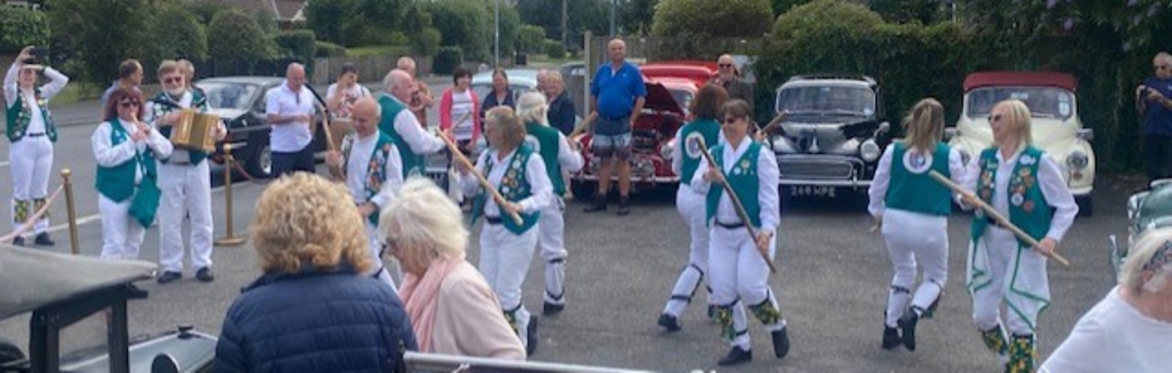 Morris dancers in green jackets and white strides with Morris Classic Cars