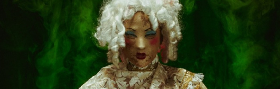 A masked gothic figure in a gown holding a blank white mask in their lap