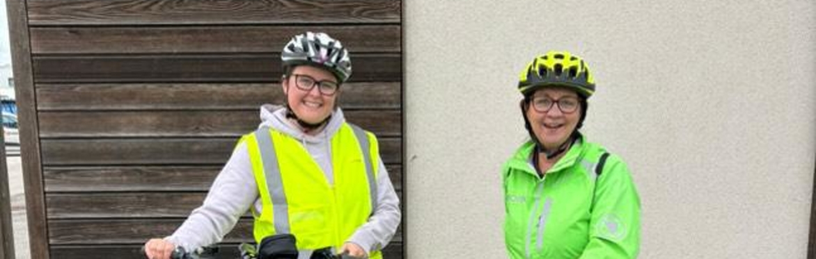 Two female cycling instructors in high vis cycle clothing are smiling after training people to ride bikes