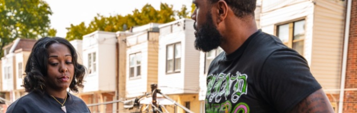 Two Black actors in a scene from digital drama comedy series A Song for Nia. One is in black and purple outfit and an all Black outfit with a colorful graphic tee.