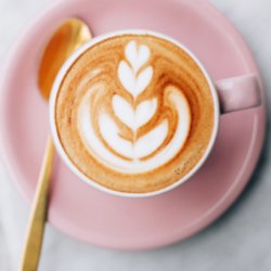 A top view of a coffee in a pink cup with coffee art of a flower