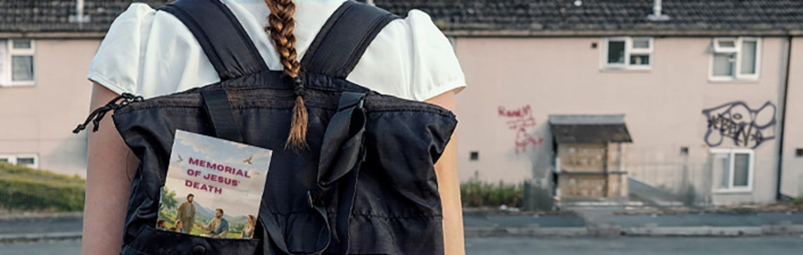 A teenage girl in school uniform looks at a row of houses. In the pocket of her backpack is a leaflet that says "Memorial of Jesus' Death"