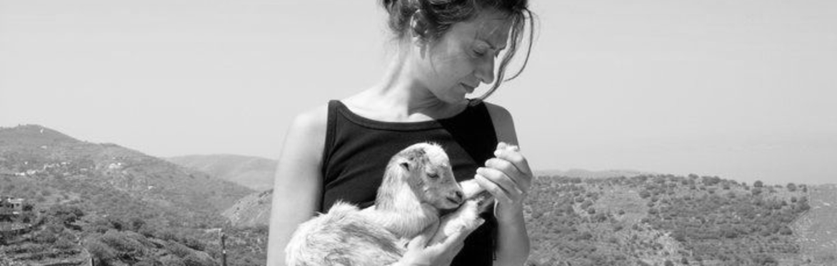 Phoebe Giannisi holds a baby goat, in front of a hilly landscape