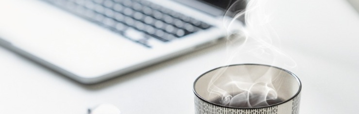 A close up of a mug of steaming tea, some spectacles, and a laptop