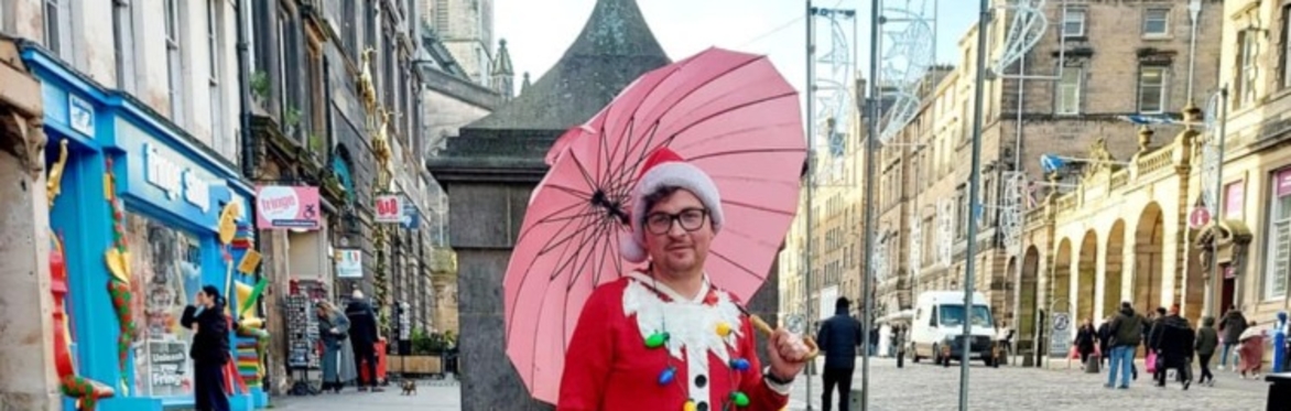 a picture of the tour guide. He is wearing a Christmas jumper that looks like a red santa suit, he is wearing a santa hat, and holding a pink umbrella