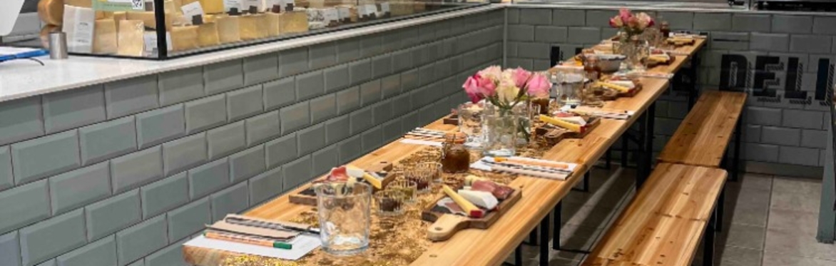 A table is laid for 10 people.  Cheeseboards are set ready for a tasting event.  Floral centrepieces add to the warm & inviting evening atmosphere.