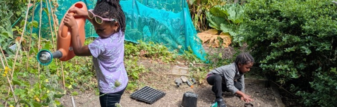 Young girl outside with a watering can and little boy digging