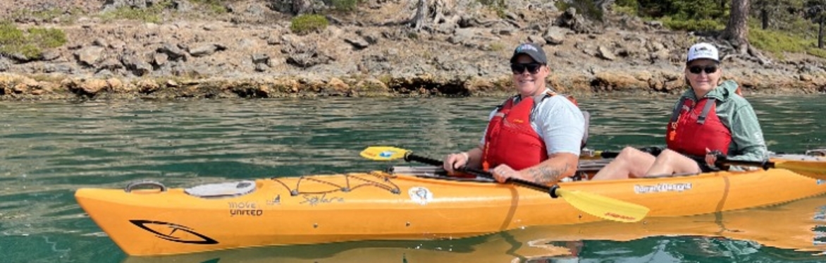 Two kayakers smile from a tandem orange kayak