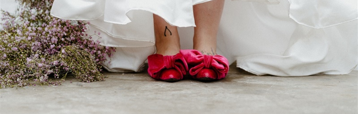 Image of a pair of feet in pink velvet shoes, with a wishbone tattoo on the model's right foot.  Image shows a locally handmade billowing dress and dried flowers