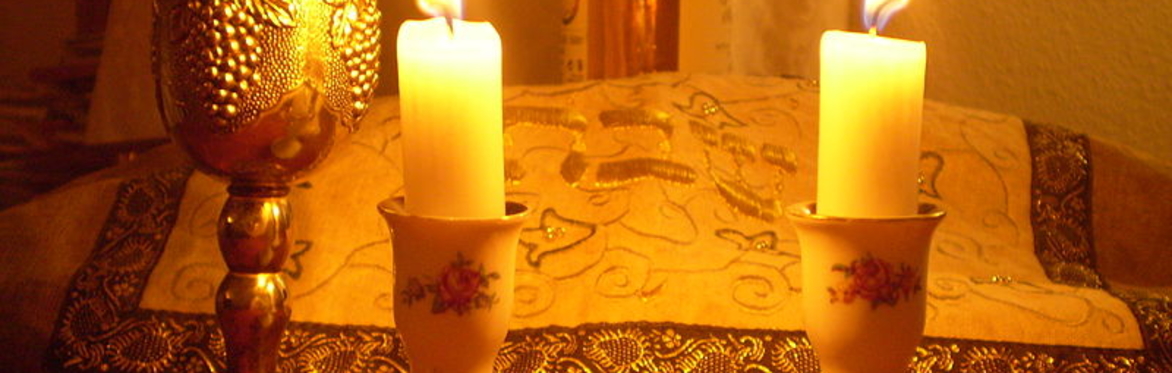photo of lit candles, kiddush cup, and hallah cover