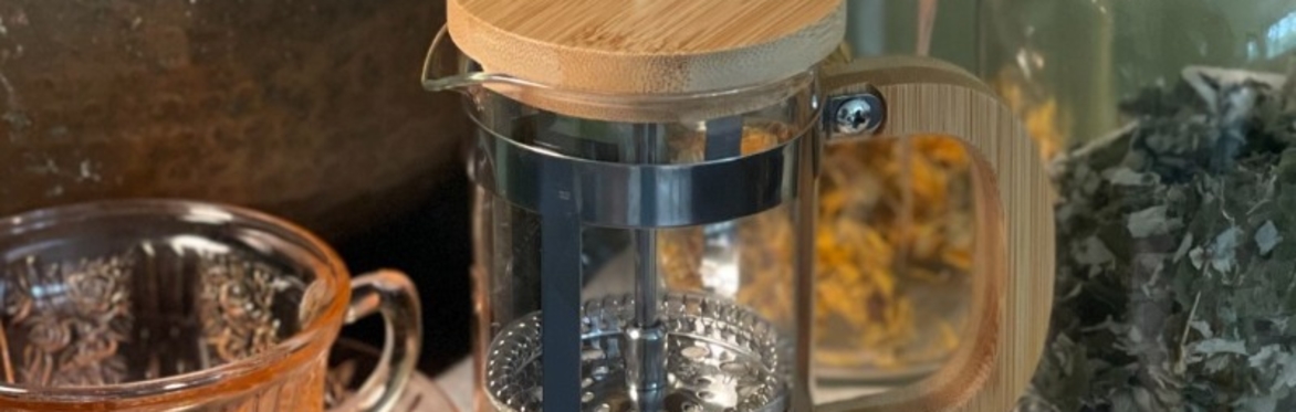 A tisane press containing dried herbs sits on a table