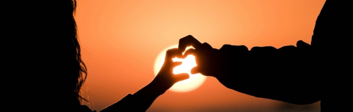 ilhouette of child and parent making heart shape with their hands as the sun is setting