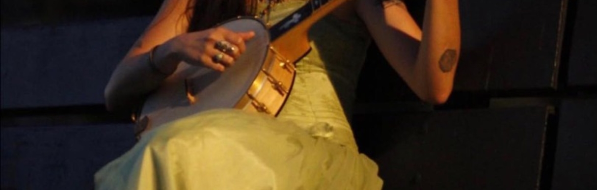 Johanna Wacker seated in a Yellow Dress Holding a Banjo while looking toward the sky.