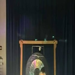 Faye sitting in front of a gong, playing crystal singing bowls