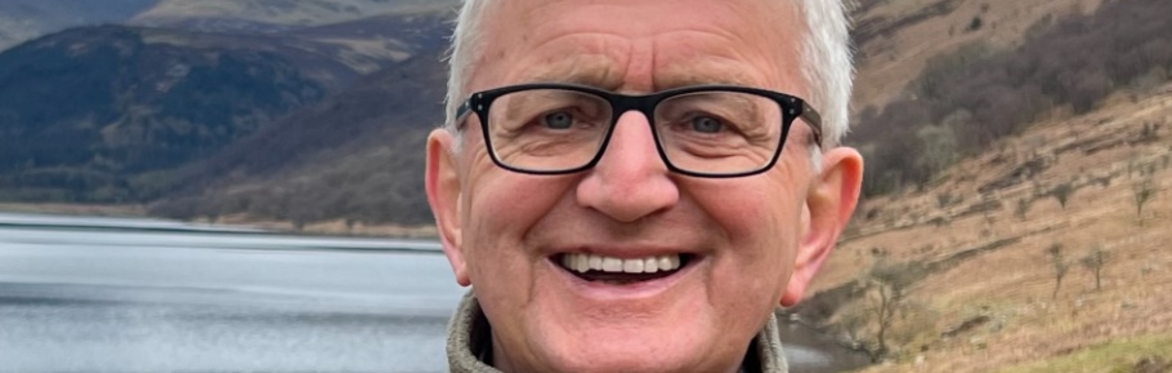 Colour picture of a head shot of Roger Crofts standing in a winter glen with hillside and a loch in the background.