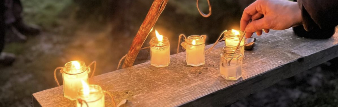 a hand lights some jam jar lanterns whilst people gather nearby