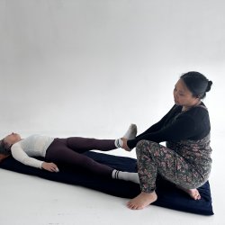 a woman lays on her back whilst another woman holds her leg in a stretch