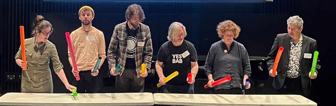 6 performers holding coloured boomwhackers over a table