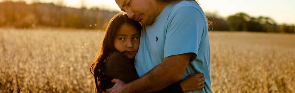 Older male embracing his young daughter in a field