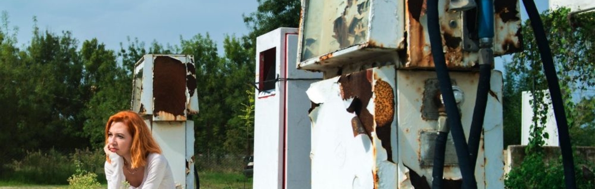Woman sitting next to derelict petrol pumps
