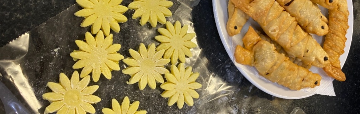 photo of beautifully crafted Bangladeshi pastries and cookies. The pastries are shaped like little fish with black eyes and are next to the yellow flower shaped cookies.