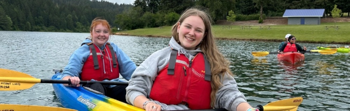 2 people paddle a tandem kayak on Hagg Lake while wearing P-F-Ds (lifejackets)