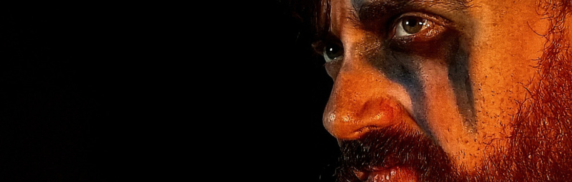 A white man holding a Viking sword, with black face paint across his left eye and cheek