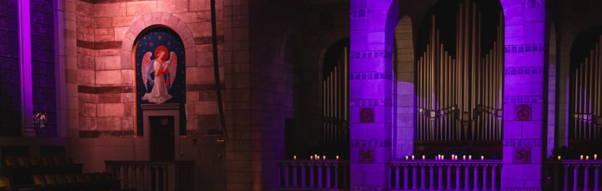 an image of the Fountain Street Church sanctuary, with the central arch lit in purple and an angel on the left lit in amber.