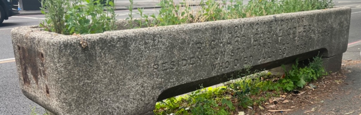 Side and end of a historic granite drinking trough for animals, with an inscription carved into the side