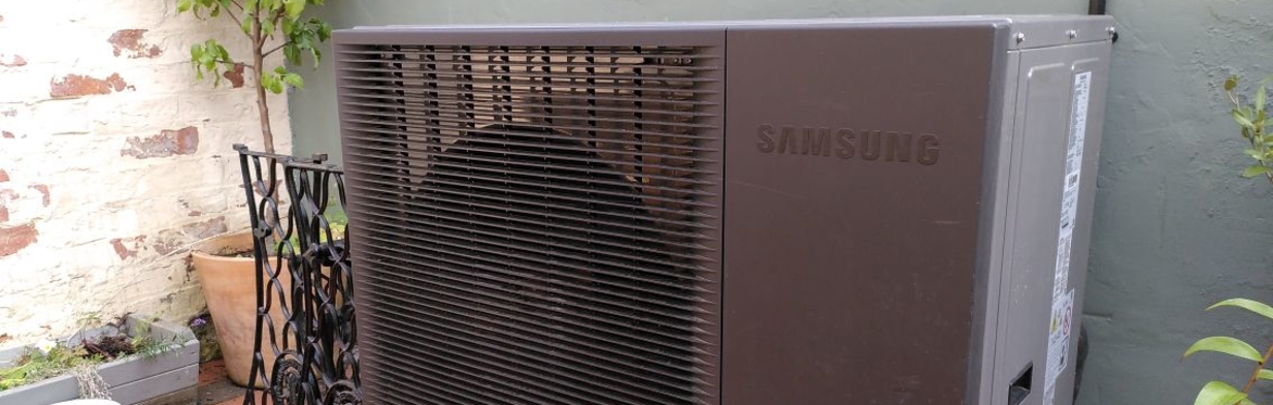 heat pump in a backyard with a potted tree next to it