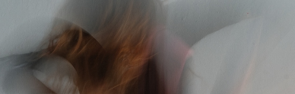 Blurred figure of a performer in motion, arms raised, creating soft, flowing movement against a light background.