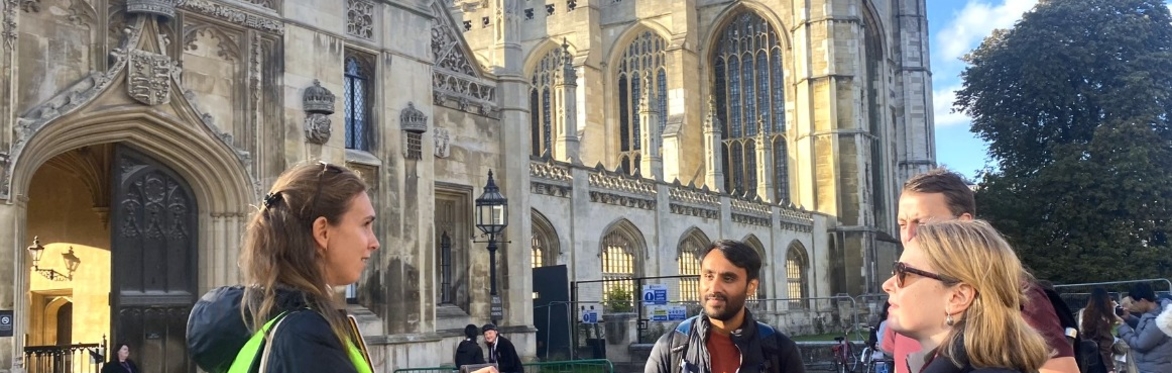 An image of an Uncomfortable Cambridge Tour, with people standing on a quiet stone street listening to a guide.
