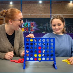 A young person and a mentor play Connect 4 together inside a youth centre.