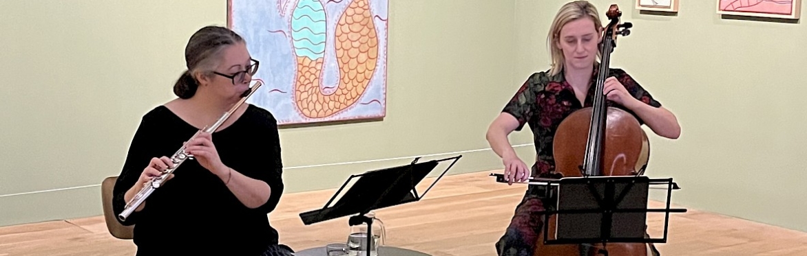 Two people performing in a gallery space, one playing the flute and the other the cello