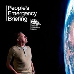 Climate activist and naturalist Chris packham looks across at a projection of the surfact of planet earth. the background is black.