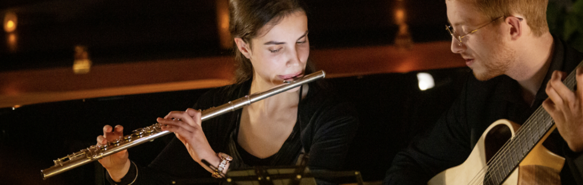 A woman with dark hair playing a flute and a man with a stringed instrument