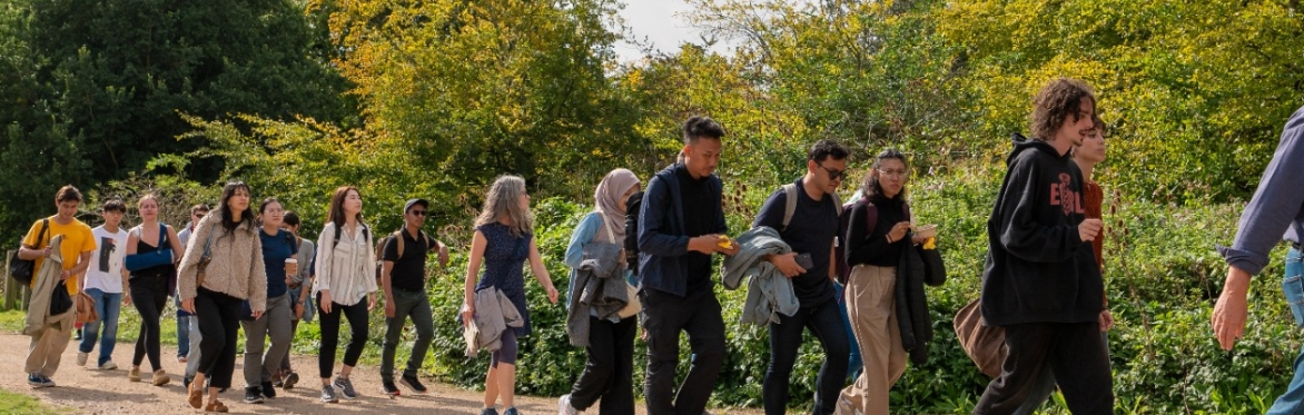A group of people walking together across the boundary of the University of Sussex campus