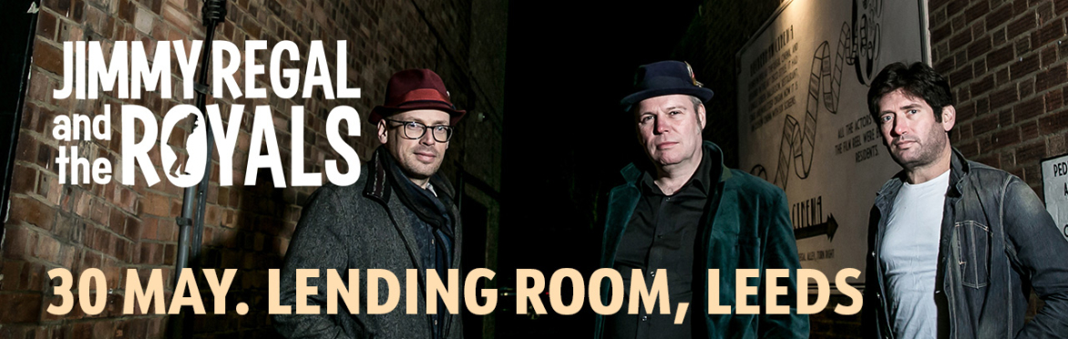 Three people stood in a well lit alley way posing for the camera. There is a sign above them in an Art Deco style that reads "Regal Alley"