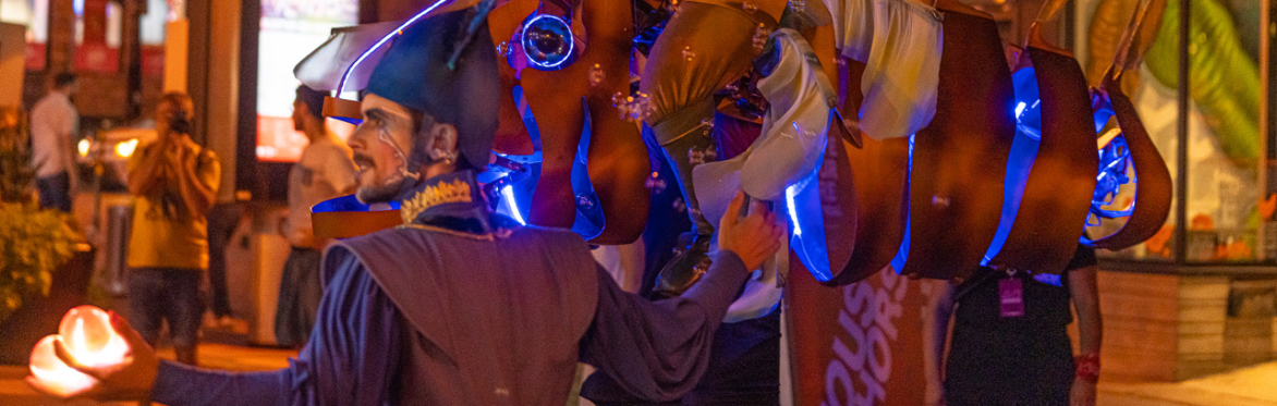 A juggler leads a glowing fish with rider through a nighttime street parade